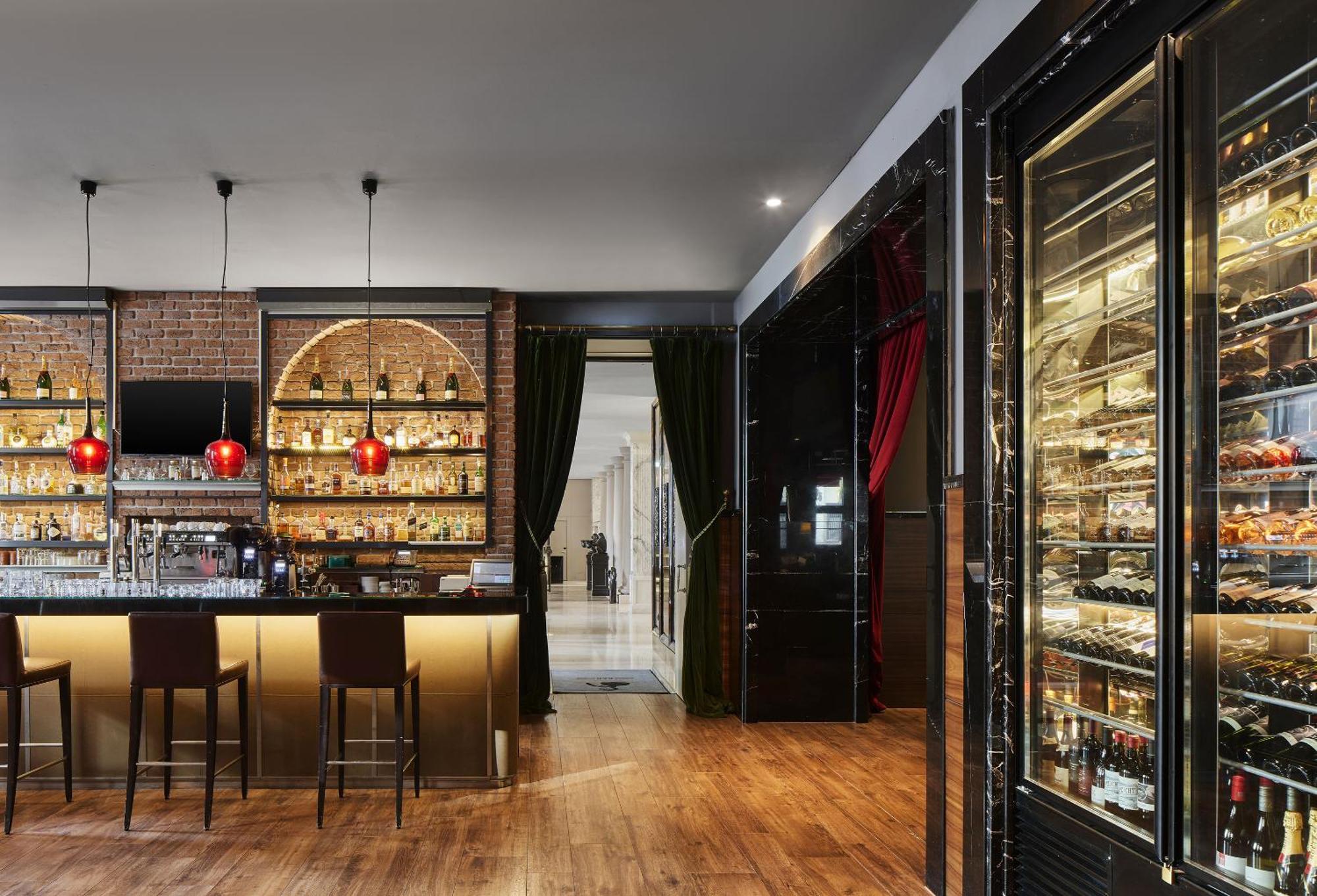 ไททานิค เกนดาร์เมนมาร์ค เบอร์ลิน โฮเทล Hotel ภายนอก รูปภาพ The photo shows a stylish bar interior. There is a sleek bar counter illuminated with warm lighting, featuring several high stools. Behind the bar, a well-stocked shelf displays various bottles of alcohol, framed by an elegant design with arched elem