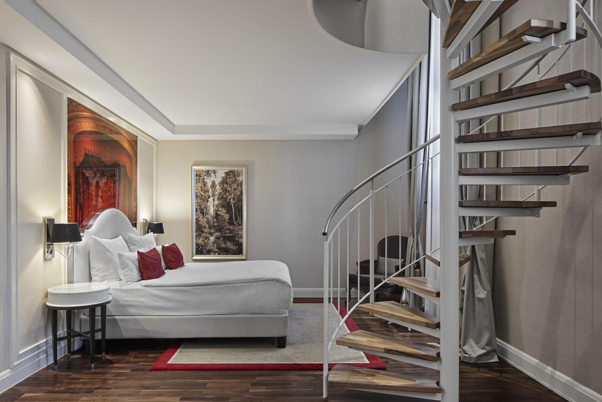 ไททานิค เกนดาร์เมนมาร์ค เบอร์ลิน โฮเทล Hotel ภายนอก รูปภาพ The photo showcases a modern bedroom featuring a queen-sized bed with a white comforter and decorative red pillows. The room has a stylish and contemporary design, with hardwood flooring and soft lighting. On the walls, there are two pieces of art: o
