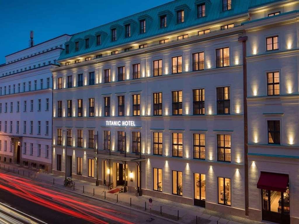 ไททานิค เกนดาร์เมนมาร์ค เบอร์ลิน โฮเทล Hotel ภายนอก รูปภาพ The photo shows the exterior of a hotel building, specifically named "Titanic Hotel." It appears to be taken during the evening, as the sky has a twilight blue hue. The hotel features a modern architectural design with large, illuminated windows that